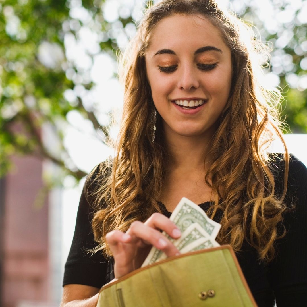 Young woman taking cash out of her wallet.